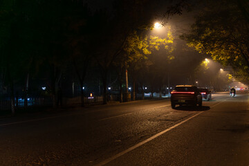 Obraz premium A long exposure of car trails creating an atmospheric night scene on a smoggy autumn night in China, showing empty city streets.