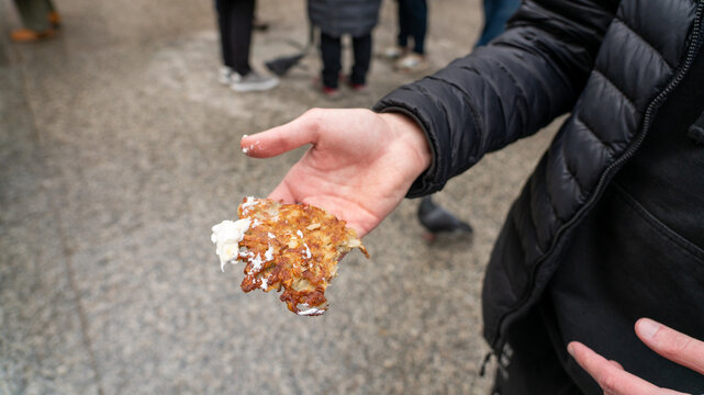 Man in Black Puffer Jacket Holding Potato Pancake with Sour Cream