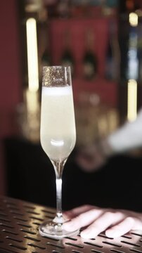 Vertical video. Barman working. Cocktail making. Unrecognizable man hand stirring alcohol drink with professional spoon in glass on bar counter.