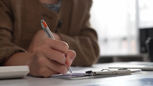 Businesswoman signing contract on clipboard at desk
