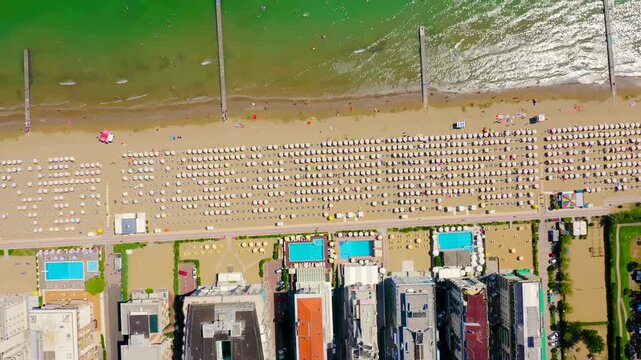 Italy, Jesolo. Lido di Jesolo, rows of white parasols and sun loungers on golden sand, aerial drone view over the Adriatic coastline with resort pools and the Venetian Riviera shoreline. Drone footag