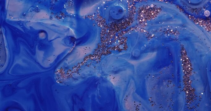 Liquid glitter flow. Shimmering art. Defocused blue color sequin bright particles floating in paint water wave on abstract background.