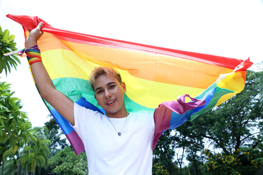 Striking portrait handsome blonde Asian gay man embracing the fluttering pride flag signifying his diverse sexual orientation and LGBTQ identity man who is attracted to other men.