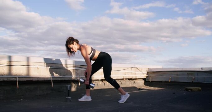 Athletic strength. Outdoor training. Active motivated woman practicing yoga energy lifting dumbbell developing endurance sportive skill on rooftop.