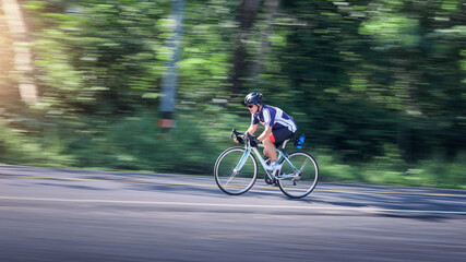 Fototapeta premium Focused cyclist riding bicycle fast on paved road near deep forest during high speed action sport training feeling completely determined