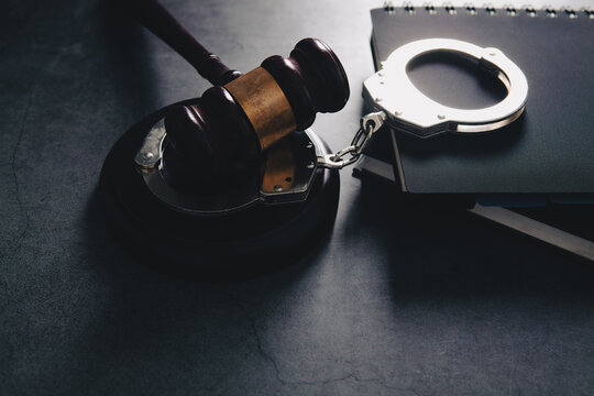 Judge gavel, handcuffs and notepad on black table background.