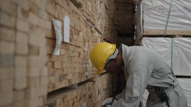 Factory Worker Inspecting Stacked Timber at Industrial Warehouse