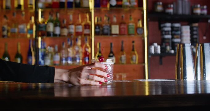 Alcohol drink. Cocktail glass. Unrecognizable customer woman hand taking beverage decorated with lemon spiral zest cherry at bar counter.