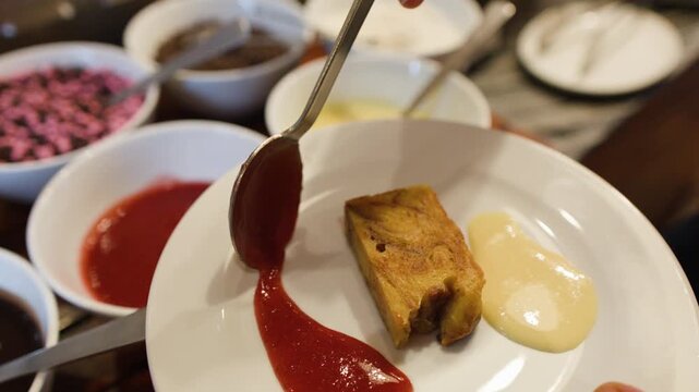 Pouring Red Strawberry Sauce onto Bread Pudding with Vanilla Custard
