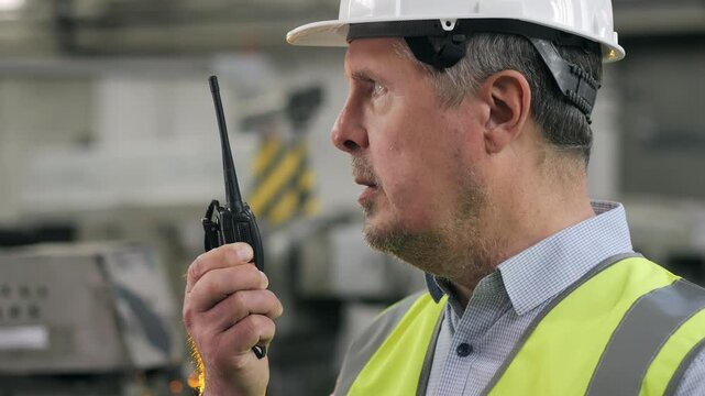 Close up of factory supervisor in hard hat using walkie talkie for communication during industrial manufacturing process.