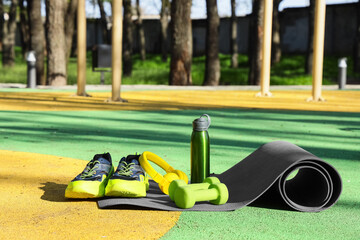 Naklejka premium Fitness mat with sneakers, headphones, water bottle and dumbbells on sports ground