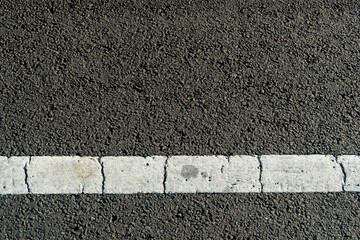Fototapeta premium Close-up depicts the texture of an asphalt road with damaged white traffic lines. The asphalt background is dark and grainy.