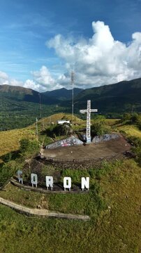 Smooth aerial pullback from cross on Mount Tapyas and Coron hillside letters in Palawan Philippines with green hills tropical valley clouds and mountain backdrop