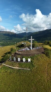 Smooth aerial push in toward cross on Mount Tapyas and Coron hillside letters in Palawan Philippines with green hills tropical valley clouds and mountain backdrop