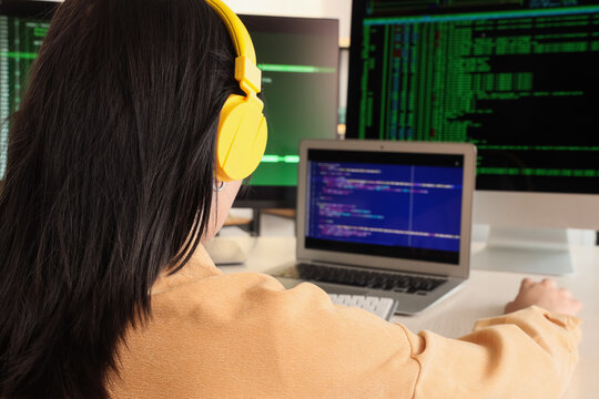 Female programmer with headphones working at desk in office, closeup