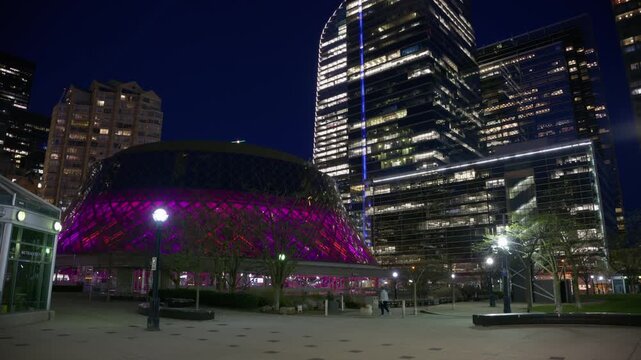 Roy Thomson Hall glowing at night in Toronto's entertainment district with modern skyscrapers illuminating King Street West in downtown Ontario, Canada's urban landscape