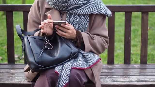 Woman sitting on bench using phone in public park