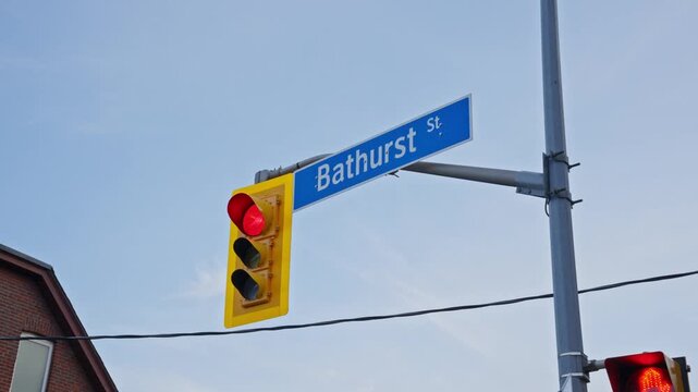 Flashing red traffic light and Bathurst Street sign in Toronto regulating urban transport and pedestrian safety with a stop signal on a clear day with blue skies