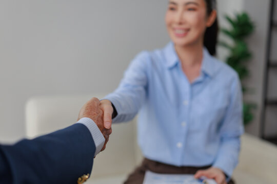 Two people are shaking hands, showcasing a moment of agreement, trust, and professional partnership as an older man and a young Asian woman finalize a successful business deal