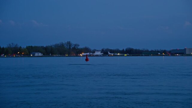 Aircraft taxiing at Billy Bishop Toronto City Airport at dusk with shimmering city lights on the horizon and calm water reflecting dark blue sky