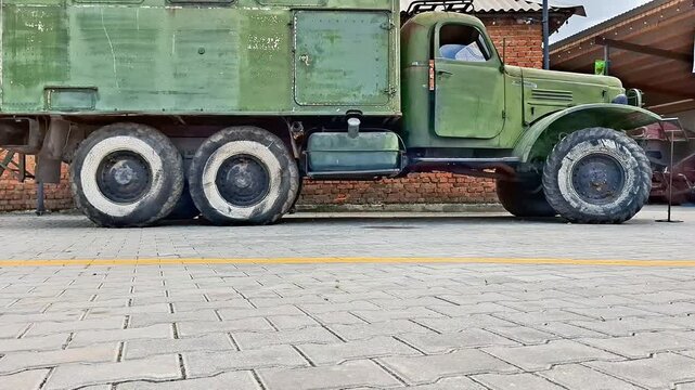 Large green six wheel military truck with boxy cargo compartment parked near brick building, showcasing rugged car, historical transport, and utilitarian field vehicle