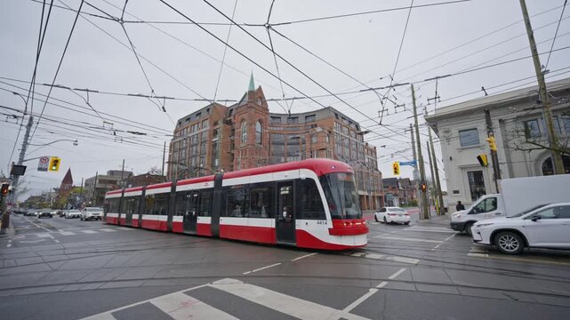 Urban public transit system showing a modern Toronto streetcar turning at city intersection with overhead power lines and historic brick buildings on overcast day