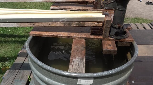 Old cast iron hand pump mounted on weather-worn wooden planks over a galvanized steel trough filled with water in a farm setting