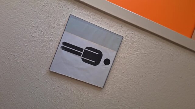 Turning sign on textured wall showing a stylized horizontal male restroom icon, black on white, slightly tilted