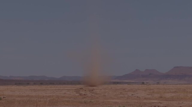 Dust devil whirlwind rising above flat arid desert plain with distant mesa Morocco