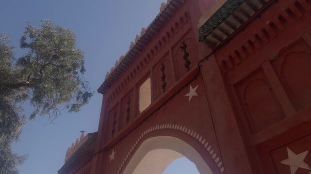 Red clay ornate Moroccan gate arch with carved star motifs and decorative cornice against blue sky