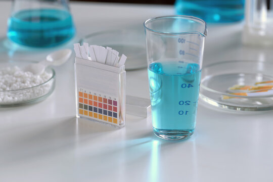 Close-up of glass flasks for chemical experiments and litmus paper against the background of other laboratory glassware.
