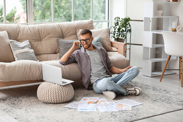 Obraz premium Young businessman in eyeglasses talking on mobile phone and working with documents on floor in office