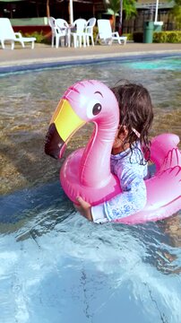 Little girl having fun swimming in inflatable ostrich ring wearing sunglasses at resort pool - Travel summer vacation