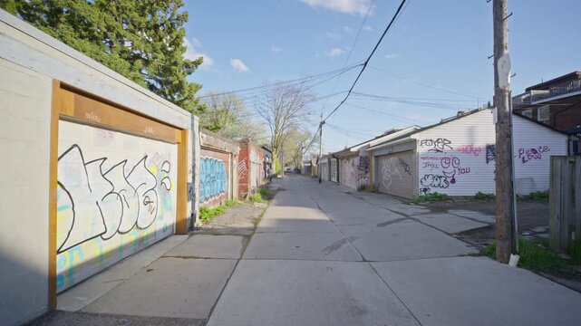 Urban landscape showcasing back alley with garage doors covered in graffiti art in a north american city, moving forward perspective