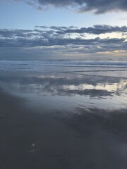 Fototapeta premium A wide angle landscape shot of glistening wet sand on the shoreline under a dramatic moody sky over the ocean in Carlsbad, California.