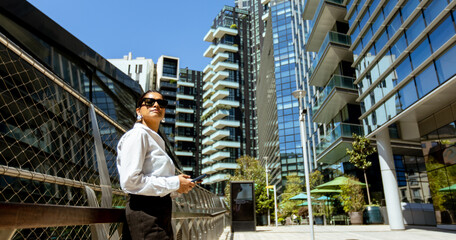 Woman stands near modern buildings on a sunny day in the city with a mobile phone © BGStock72