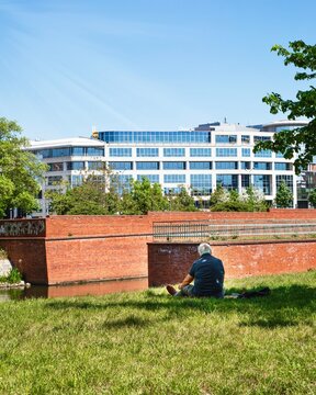 Poland, Wroclaw, 10.05.2026. Man relaxing on grass near river with Bema Plaza building in Wroclaw Poland