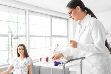 Fototapeta premium Female doctor preparing young donor for blood transfusion in clinic