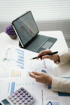 Business professional reviewing financial reports and performance charts at a modern office desk, analyzing data, planning strategy, and managing corporate documentation.