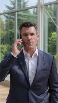 Middle-aged businessman on phone in modern glass greenhouse, vertical footage