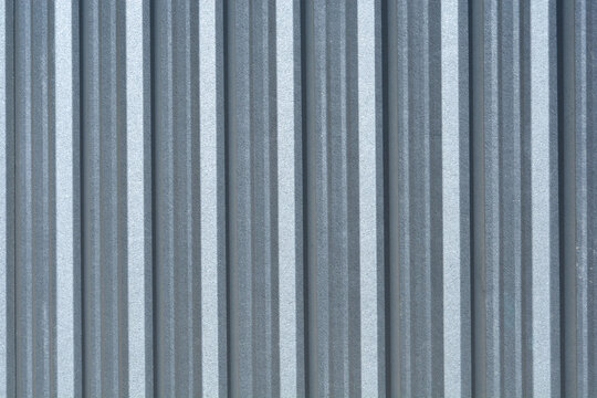 A full frame background texture of a grey corrugated zinc metal sheet with vertical ridges used for industrial fencing or roofing