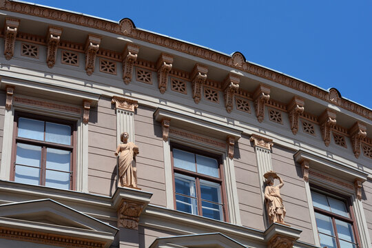 Detailed view of a classic historical building facade decorated with two elegant female stone statues and decorative roof trims against a blue sky in Zagreb, Croatia
