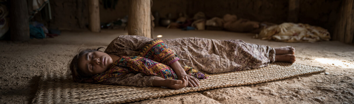 A Child's Slumber in a Rustic Dwelling: A young child sleeps soundly on a woven mat within a simple, rustic dwelling. The soft light filtering into the room illuminates the peaceful scene.