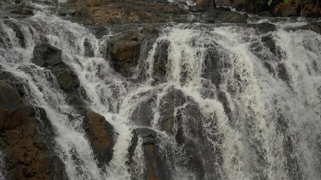Static slow motion close-up of Tad Khoo waterfall cascading over dark rocks, with a subtle zoom effect on the flowing water.