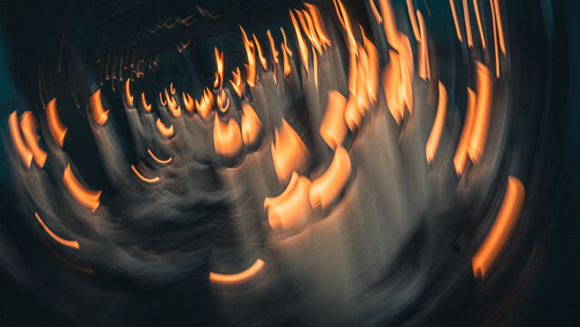 Creative circular motion blur of burning candles with orange flames against dark teal background