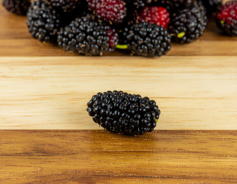 Selective focus illustration of a single ripe black mulberry on a wooden table with blurred background