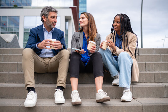 Diverse business people sharing coffee break on city stairs