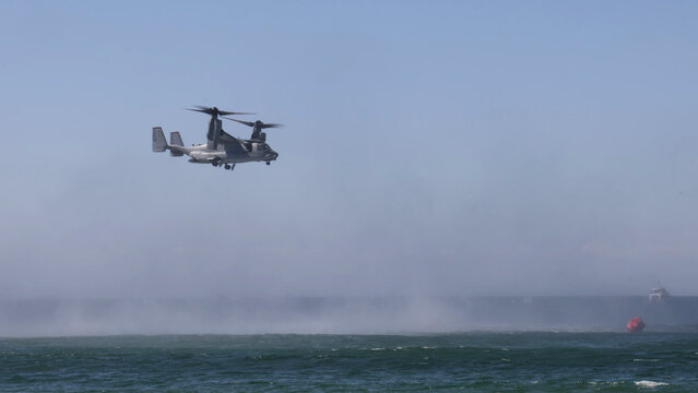 Military Tiltrotor Aircraft Hovering Low Over Ocean Creating Water Spray