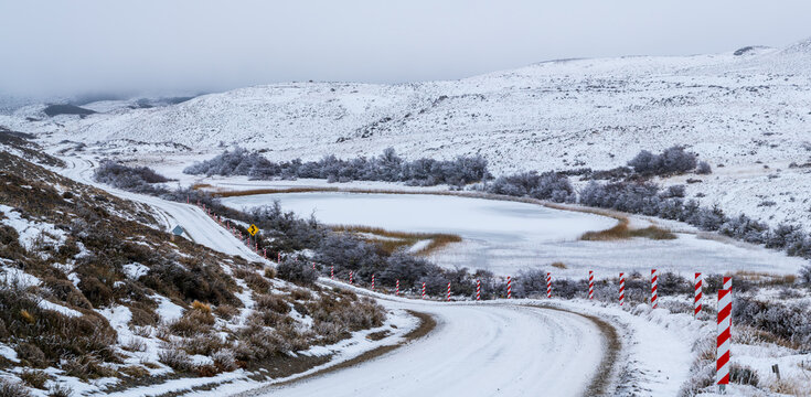Panoramic view of a snowcovered gravel road with red and white safety posts near a frozen lake in winter Torres del Paine National Park Patagonia Chile