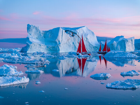 Segelboote mit roten Segeln zwischen Eisbergen in Ilulissat in Gr&ouml;nland in der wundersch&ouml;nen, bunten und romantischen Mitternachtssonne
 
